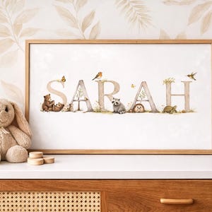 May include: A framed print featuring the name "SARAH" in decorative letters. Each letter is adorned with woodland creatures and floral accents. The artwork is set against a neutral background, creating a charming nursery or children's room decor.
