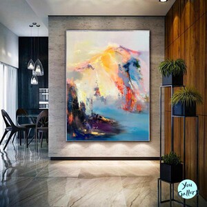 May include: Abstract painting of a mountain range with vibrant colors, including yellow, orange, red, blue, and purple. The painting is displayed in a modern home setting.