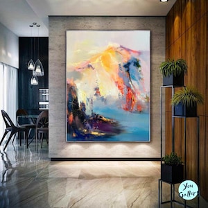 May include: Abstract painting of a mountain range with vibrant colors, including yellow, orange, pink, blue, and purple. The painting is displayed on a wall in a modern home.