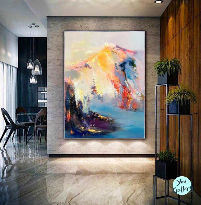 May include: Abstract painting of a mountain range with vibrant colors, including yellow, orange, pink, blue, and purple. The painting is displayed on a wall in a modern home.