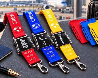 Puede incluir: Tres cordones de tela en rojo, azul y amarillo, cada uno con una hebilla de cinturón de seguridad de avión de metal, el texto CREW, un icono de globo terráqueo y la frase TO FLY IS TO LIVE. Los cordones muestran los logos de Jet2, TUI y Ryanair.