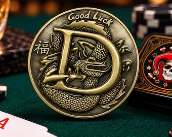 May include: A round, antique-finish brass coin featuring a large letter D embossed over a detailed dragon. The coin includes the text Good Luck and a Chinese character. It is positioned among playing cards, poker chips, and a glass of amber liquid.