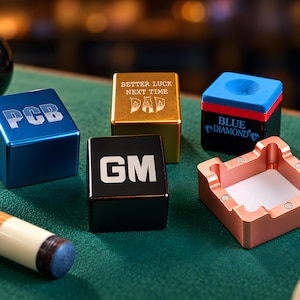 Könnte beinhalten: Eine Sammlung von Billardkreidehaltern, bestehend aus einem blauen Würfel mit PCB, einem goldenen Würfel mit BETTER LUCK NEXT TIME DAD, einem schwarzen Würfel mit GM, einem Blue Diamond Kreidewürfel und einem roségoldenen Magnethalter mit vier Magneten.