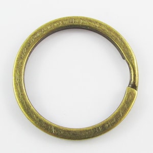 May include: A gold-toned metal key ring with a split ring opening. The ring is oval shaped and has a smooth, polished finish.