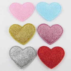 May include: Six heart-shaped embellishments with a glitter finish. The hearts are in pink, light blue, gold, pink with glitter, silver with glitter, and red with glitter.