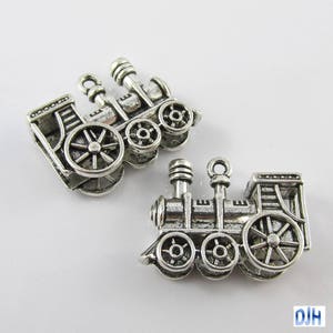 May include: Two silver-toned metal train engine charms. The charms are detailed with wheels, smokestacks, and windows.