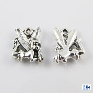 May include: Two silver charm pendants featuring a cartoon fairy with wings. The fairy is in a flying pose with its arms outstretched.