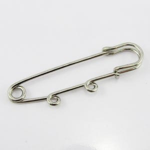 May include: Silver safety pin with three loops on the bar. The pin is designed for attaching fabric or other materials.