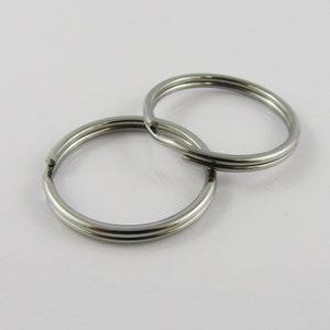 May include: Two silver key rings, one slightly larger than the other, are shown on a white background. The rings are made of metal and have a smooth, polished finish.