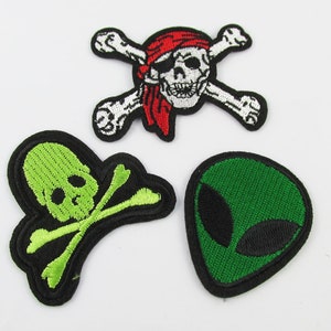 May include: Three embroidered iron-on patches. One patch features a green skull and crossbones. Another patch features a green alien head. The third patch features a white skull and crossbones with a red bandana.