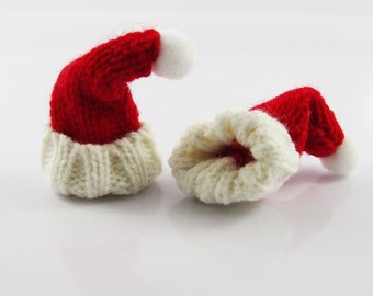 May include: Two miniature knitted Santa hats, one red with white trim and a white pom-pom, the other turned inside out to show the white knit lining.