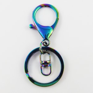 May include: A rainbow-colored metal keychain clasp and ring set. The clasp is a lobster claw style, and the ring is a split ring. The set is made of metal with a shiny, iridescent finish, reflecting a spectrum of colors.