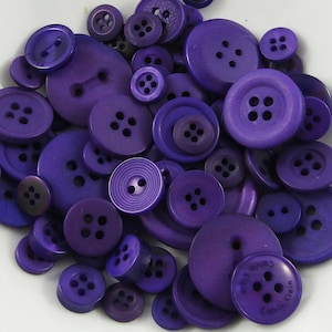 May include: A collection of purple buttons in various sizes and styles. The buttons are made of plastic and have a smooth, shiny finish.