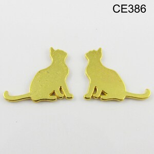 Puede incluir: Dos abalorios de metal de color dorado en forma de silueta de gato. Los gatos est&aacute;n sentados con las colas enroscadas alrededor de sus cuerpos.