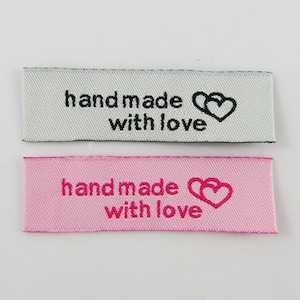 May include: Two fabric labels with the text "handmade with love" and a double heart symbol. The top label is white with black text and the bottom label is pink with pink text.