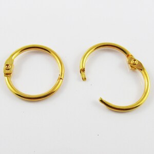 May include: Two gold metal binder rings, one open and one closed. The rings are designed to hold papers together.