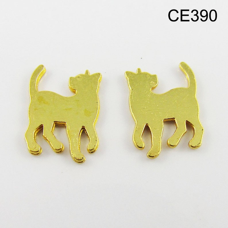Puede incluir: Dos abalorios de metal dorado en forma de gato, cada uno con una silueta detallada de un gato de pie sobre sus cuatro patas. Los abalorios son id&eacute;nticos y tienen un acabado liso y brillante.