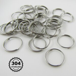 May include: A pile of silver-coloured split key rings. The rings are made of stainless steel and are open, ready for use. The image includes a circular emblem that reads "304 STAINLESS".