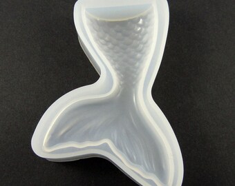 May include: A white silicone mold shaped like a mermaid tail. The mold has a detailed design of scales on the tail.