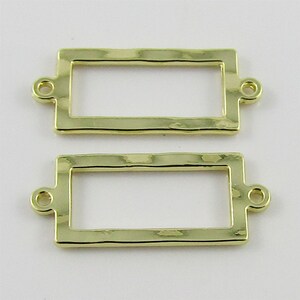 May include: Two gold-toned metal rectangular frames with a hammered texture. Each frame has two small loops at the top for attaching to a necklace or bracelet.