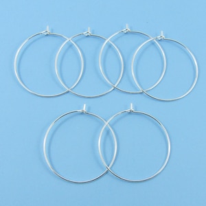 May include: Six silver hoop earrings, each with a simple circular design. The earrings are arranged in two rows of three, with the top row slightly offset from the bottom row.