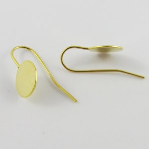 May include: A pair of gold-toned earring blanks with a round disc at the bottom. The earring blanks are made of metal and have a simple design.