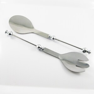 May include: A set of two silver serving utensils with decorative handles. The utensils are a spoon and a fork.