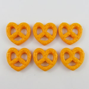 May include: Six orange heart-shaped pretzel charms. The pretzels have a knot design in the center.