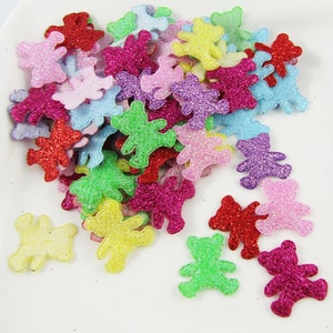 May include: A pile of colourful glitter teddy bear shapes. The bears are in various colours including pink, purple, green, yellow, red, and blue.