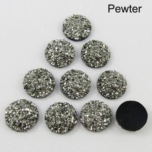 Puede incluir: Diez cabujones redondos de color plateado, cubiertos de purpurina, cada uno mide aproximadamente 2,5 cm de di&aacute;metro. Los cabujones est&aacute;n dispuestos en forma triangular sobre un fondo blanco. La palabra "Pewter" est&aacute; escrita en negro en la parte superior de la imagen.