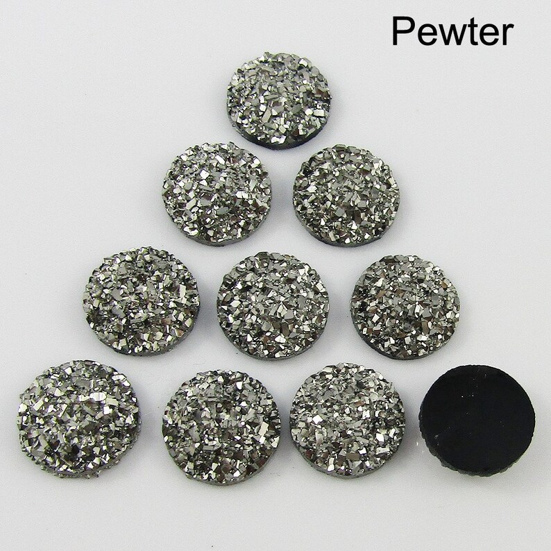 Puede incluir: Diez cabujones redondos de color plateado, cubiertos de purpurina, cada uno mide aproximadamente 2,5 cm de di&aacute;metro. Los cabujones est&aacute;n dispuestos en forma triangular sobre un fondo blanco. La palabra "Pewter" est&aacute; escrita en negro en la parte superior de la imagen.