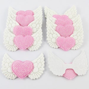 May include: A set of ten pink glitter heart with white wings embellishments. The hearts are approximately 1.5 inches in diameter.