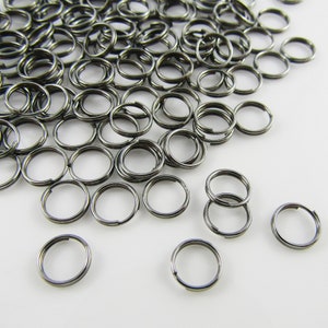 May include: A large pile of black metal jump rings. The rings are small and round, and they are all piled together in a heap. There are a few rings that are separated from the pile.