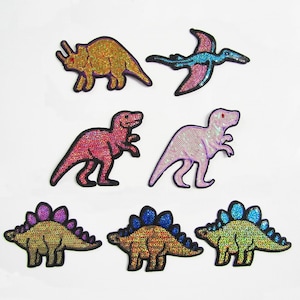 May include: Set of eight iron-on patches featuring various dinosaurs, including a triceratops, pterodactyl, stegosaurus, and tyrannosaurus rex. The patches are made of iridescent sequins and come in a variety of colours, including pink, blue, gold, and purple.