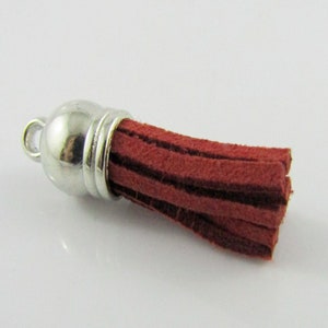 May include: A small, red suede tassel with a silver metal cap and a loop for attaching to a keychain or other item.