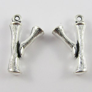 Op de afbeelding: Twee zilveren metalen bedels in de vorm van takken met een lus aan de bovenkant om te bevestigen aan sieraden of andere knutselwerkjes.