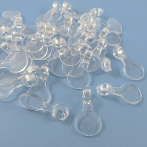 May include: A pile of clear plastic garment loop fasteners. The loops are small and have a round base with a small loop extending from the top.