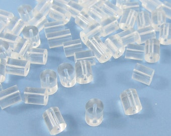 May include: A collection of clear, cylindrical earring backs. Each back has a small hole running through the center. The earring backs are scattered on a light blue surface, creating a simple, clean aesthetic.