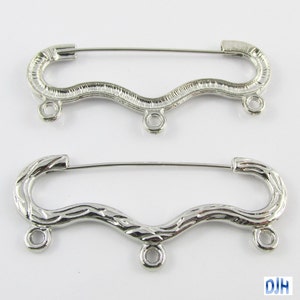 May include: Two silver-toned metal safety pin closures with three jump rings. The top closure has a smooth, wavy design. The bottom closure has a textured, wood-grain design.