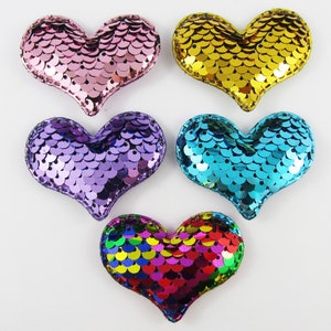 May include: Five heart-shaped sequins in different colours: pink, gold, purple, blue, and rainbow. Each heart is sewn with a decorative stitch around the edges.