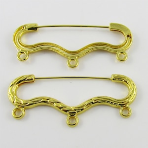May include: Two gold-toned safety pin style clasps with three jump rings each. The clasps are wavy and one has a textured design.