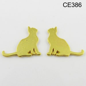 Puede incluir: Dos abalorios de metal de color dorado en forma de silueta de gato. Los gatos est&aacute;n sentados con las colas enroscadas alrededor de sus cuerpos.