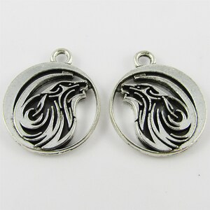 May include: Two silver-toned metal charms in the shape of a wolf's head inside a crescent moon. The wolf's head is detailed with intricate lines and the moon is smooth.