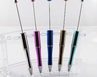 Puede incluir: Cinco bolígrafos metálicos con cuerpos de diferentes colores, incluyendo plateado, rosa, azul, dorado y turquesa, se muestran en un soporte de plástico transparente.