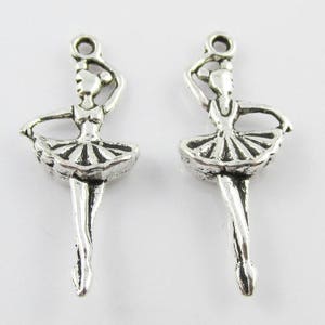 May include: Two silver ballerina charm pendants with a detailed design. The ballerina is wearing a tutu and has her arms outstretched.