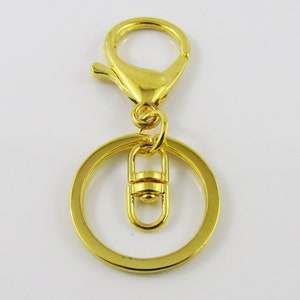 May include: Gold-toned metal key chain with a round ring and a spring clasp. The ring has a smaller, spring-loaded loop attached to it.