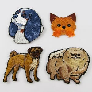 May include: Four embroidered dog patches. The patches include a blue and white Cavalier King Charles Spaniel, an orange Yorkshire Terrier, a tan Pug, and a tan Pomeranian. Each patch is detailed with various colours and textures.