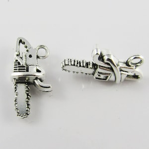 May include: Two silver charm pendants shaped like chainsaws. The charms have a detailed design and are ready to be added to a necklace or bracelet.