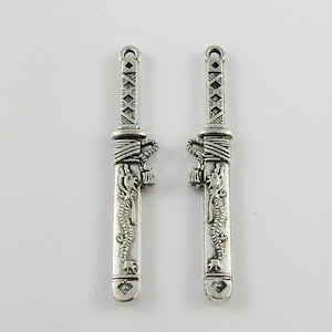 May include: Two silver-toned metal charms shaped like Japanese swords with dragon designs. The swords have a black and white rope detail at the hilt.
