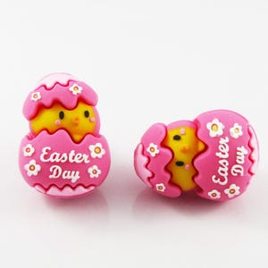 May include: Two pink Easter egg charms with a yellow chick peeking out of the top. The eggs have white flowers and the text "Easter Day" on them.